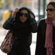 Women adjust their headscarves as they walk along a sidewalk in Tehran.